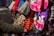 A variety of colorful knitted and crocheted items are displayed. The collection includes hats, mittens, and bags with heart and animal designs. A person’s arm is extended, touching one of the items.