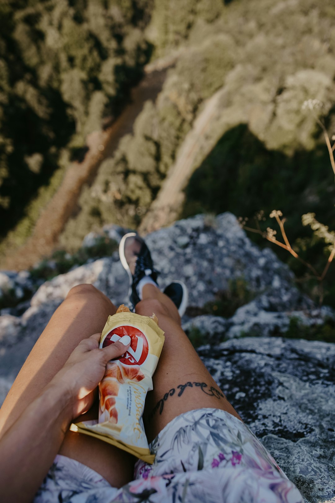 person holding white labeled plastic pack sitting on cliff during daytime