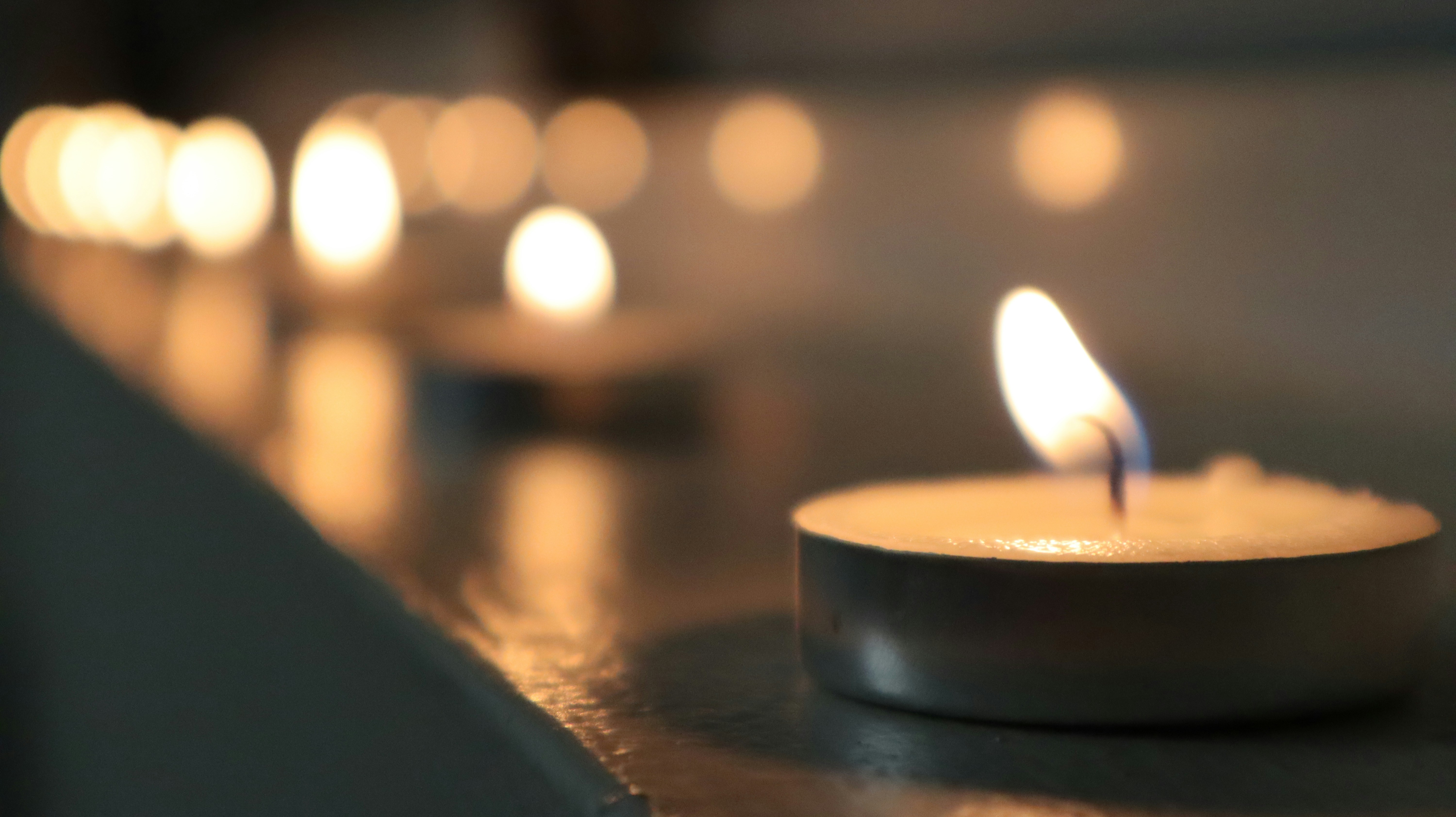 Single candle flame in darkness, warm amber light against deep black background, intimate and sacred