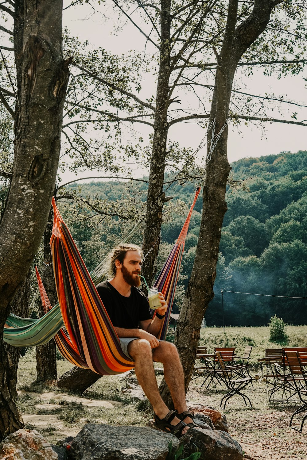 man sitting on hammock while drinking during daytime