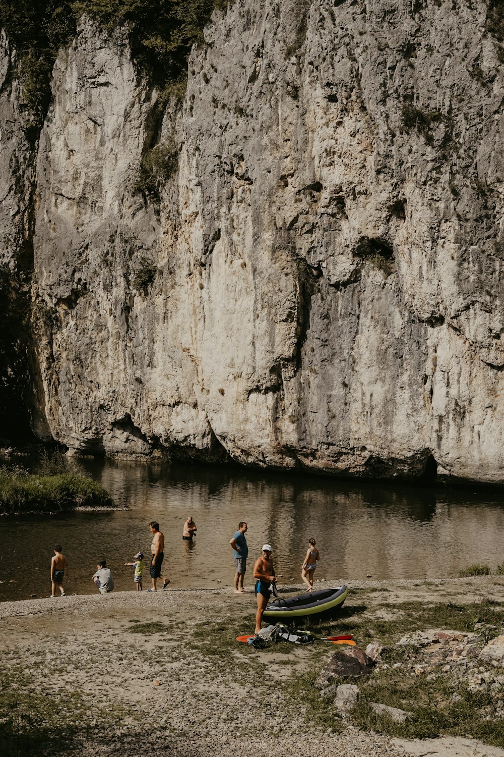 people bathing at river by the rock wall cliff