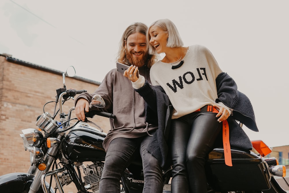 donna e uomo che si siedono sulla motocicletta mentre tengono il telefono