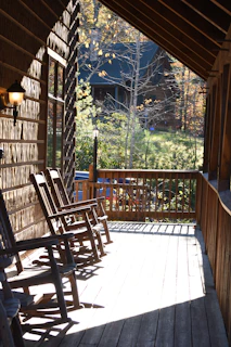 Rustic cabin porch with rocking chairs and forest views.