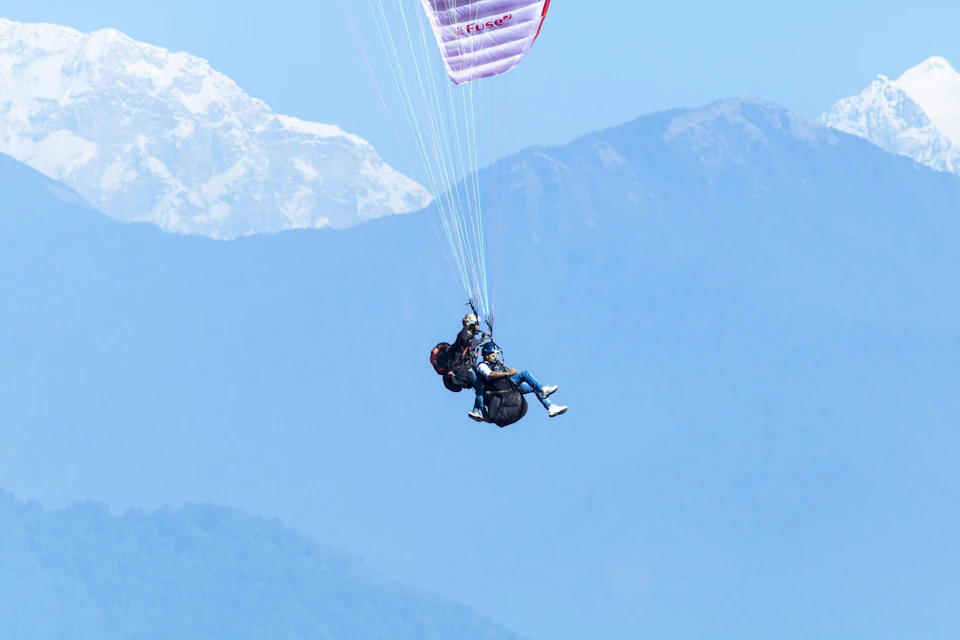 Person wearing black helmet and harness suspended in mid-air attached to parachute canopy