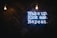A motivational quote in neon sign format is displayed against a dark wooden background. Two bright light bulbs hang from the top, illuminating the space with a warm glow. The neon text is vibrant and eye-catching, conveying a message of determination and action.