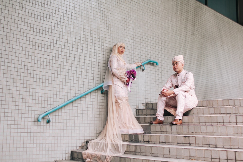 man sitting on stairs in front woman standing beside stair railing