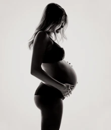 A pregnant woman in silhouette holding her belly against a bright white background