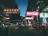 A bustling city street at dusk with colorful neon signs and blurred motion of pedestrians.