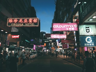 A city street at dusk glowing with orange and blue neon signs reflecting on wet pavement.