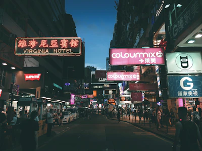 A bustling city street at dusk with colorful neon signs and blurred motion of pedestrians.