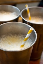 Three metal cups filled with a frothy liquid and each containing a yellow and white striped straw. The cups are arranged closely together, creating a casual and inviting atmosphere.