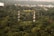 Two communication towers stand amidst a dense forest with lush green trees. In the background, a cityscape with buildings is visible, providing a contrast between nature and urban development.