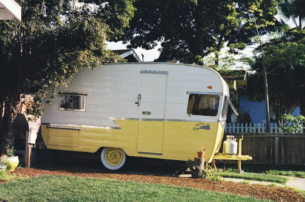 Trailer de viagem branco e amarelo estacionado ao lado da cerca