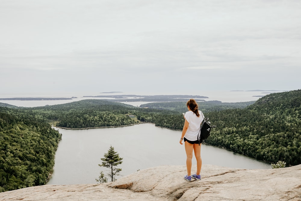 woman standing on rock formation in front of lake