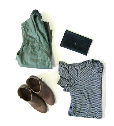 A neatly arranged display of clothing and accessories, including a folded green jacket, a pair of brown ankle boots, a black clutch, and a striped black and white shirt.