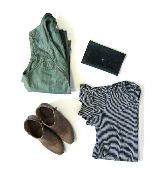 A neatly arranged display of clothing and accessories, including a folded green jacket, a pair of brown ankle boots, a black clutch, and a striped black and white shirt.