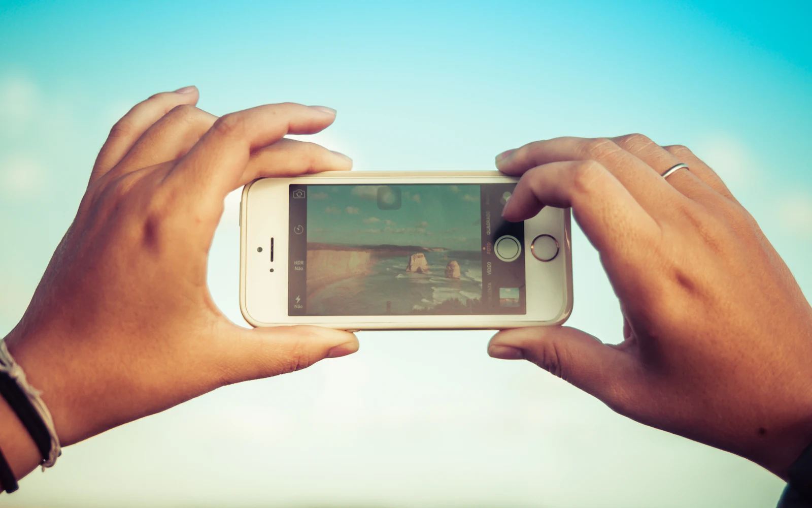 Two hands holding a phone up against a pale blue sky.