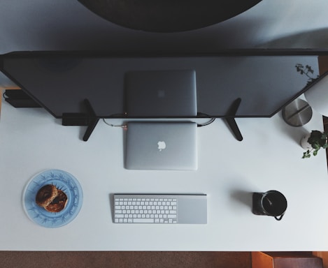 A clean, minimal workspace with a laptop, notebook, and purple taskir logo on a white desk.