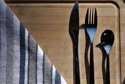 A polished set of luxury cutlery shining under soft light on a textured wooden cutting board.
