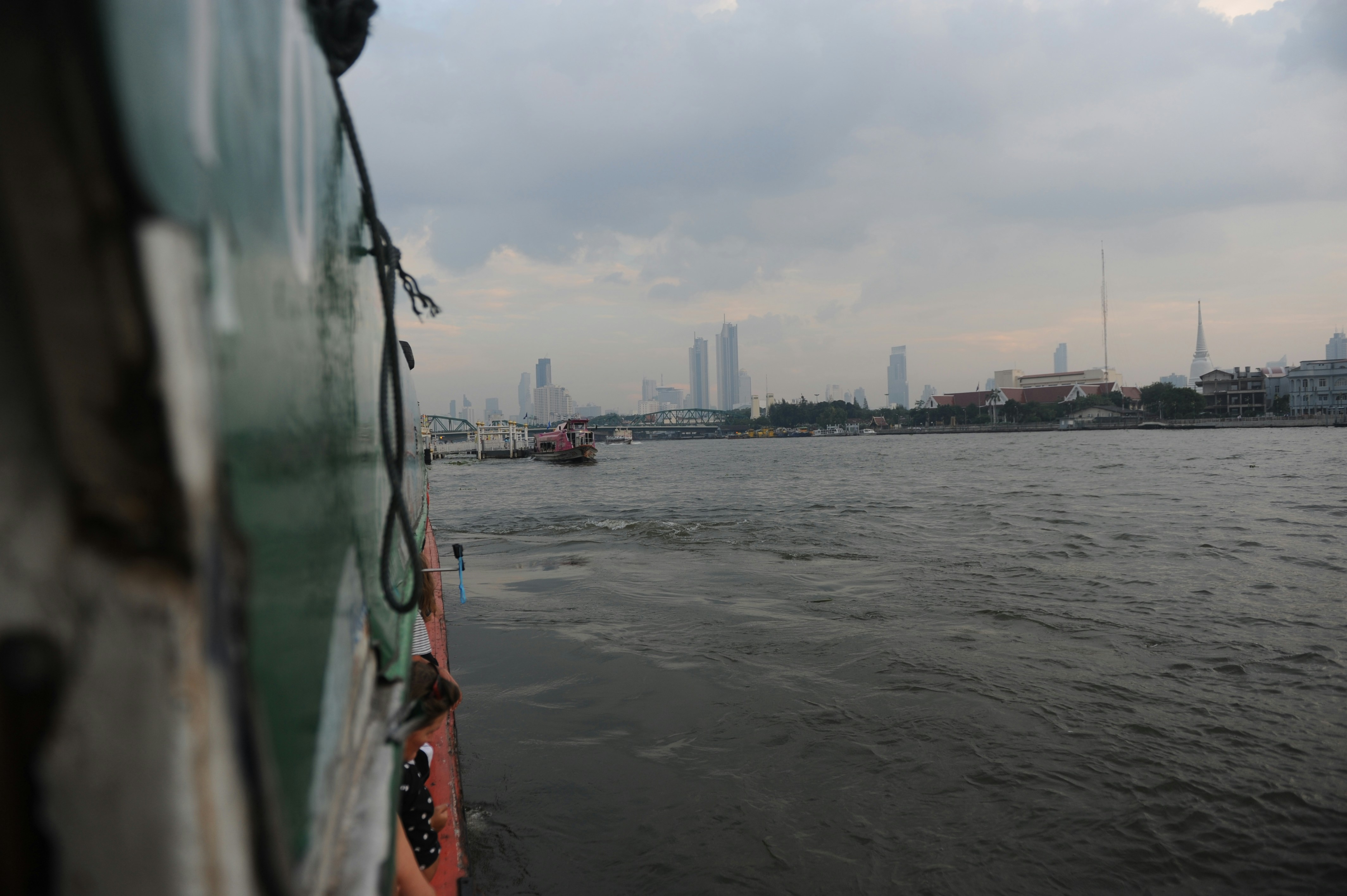 A passenger boat travels on a river through central Bangkok.