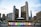 A modern cityscape featuring a large, brightly lit sign spelling 'TORONTO' with a multi-colored letter and a maple leaf symbol. Behind the sign, tall office buildings, including a distinctive curved twin tower structure, are visible under a partly cloudy sky.
