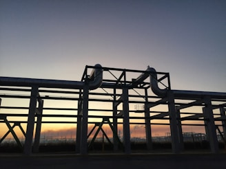 Sunset view over a refinery plant with pipes and storage tanks silhouetted.