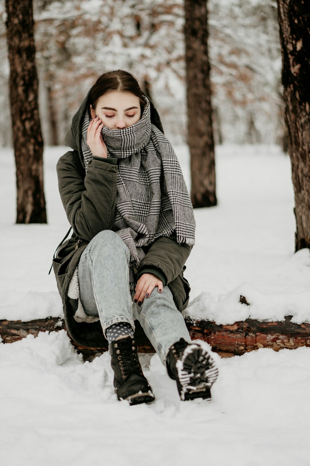 Donna che indossa una sciarpa grigia seduta sull'albero caduto coperto di neve