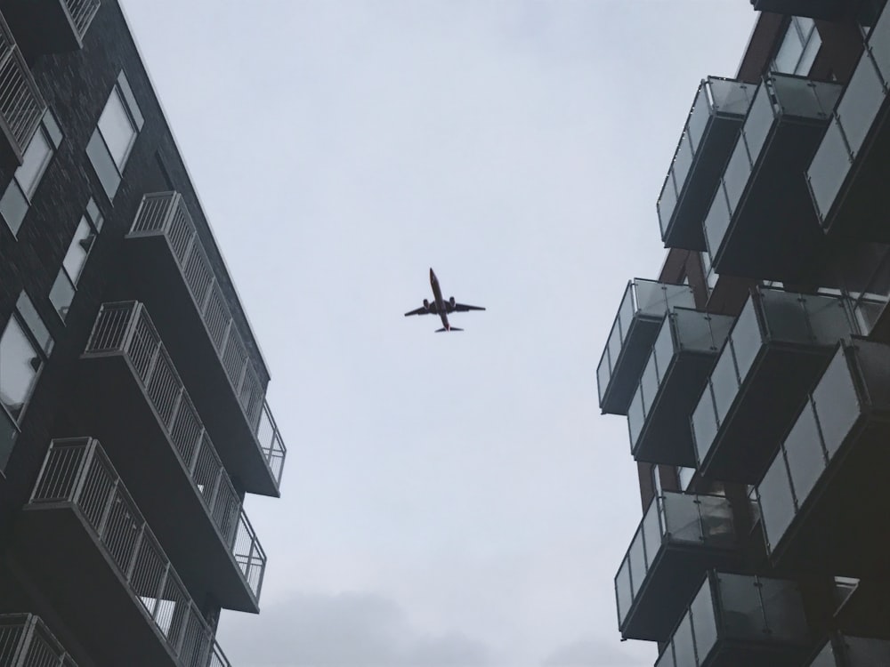 low-angle photography of airplane in flight over buildings