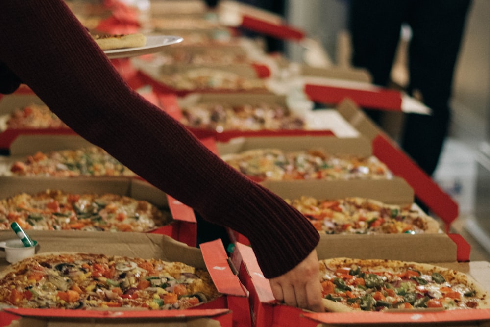 person reaching of a pizza on other side of table