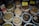 Various types of dried herbs and roots are displayed in large, open plastic bags, each containing a different kind of herb or root. Some bags have labels with prices written in Chinese characters. The image is likely taken in an herbal market or shop.