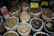 Various types of dried herbs and roots are displayed in large, open plastic bags, each containing a different kind of herb or root. Some bags have labels with prices written in Chinese characters. The image is likely taken in an herbal market or shop.
