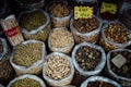 Various types of dried herbs and roots are displayed in large, open plastic bags, each containing a different kind of herb or root. Some bags have labels with prices written in Chinese characters. The image is likely taken in an herbal market or shop.