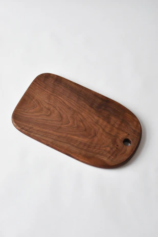 Close-up of a handcrafted oak cutting board with engraved personalized initials on a warm beige linen surface.