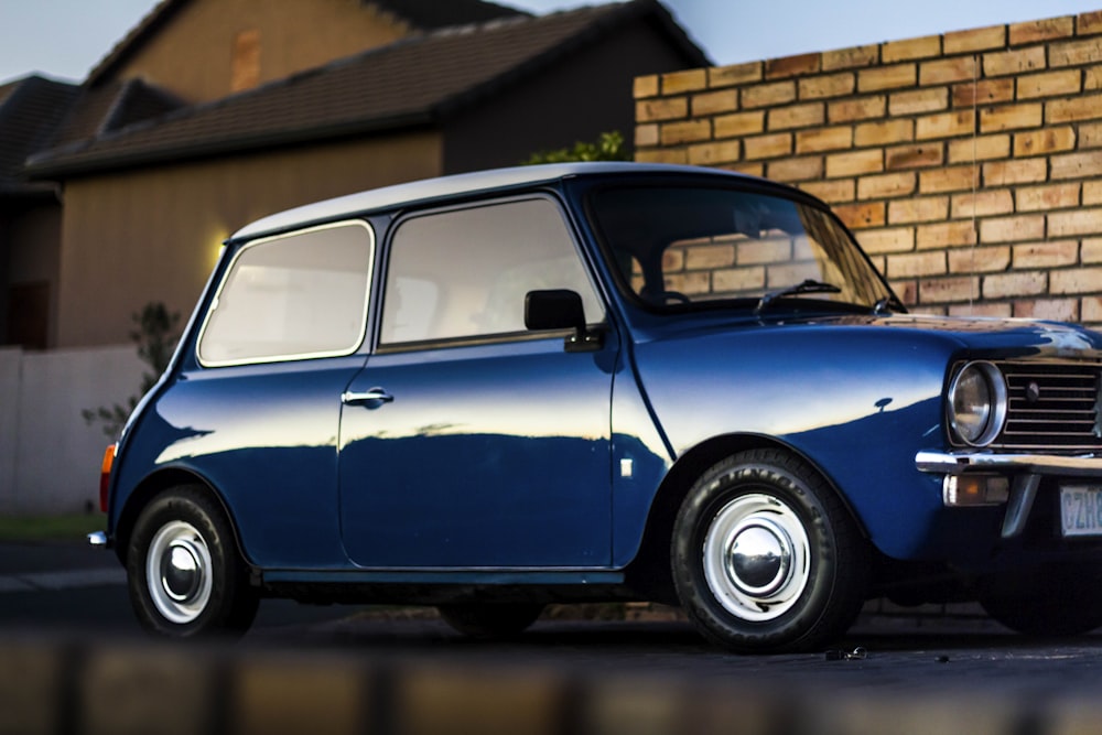 blue 3-door hatchback parking beside bricks wall