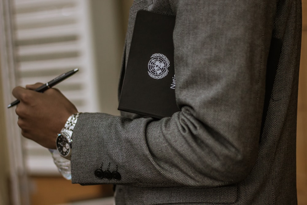 hombre sosteniendo un libro negro y un bolígrafo