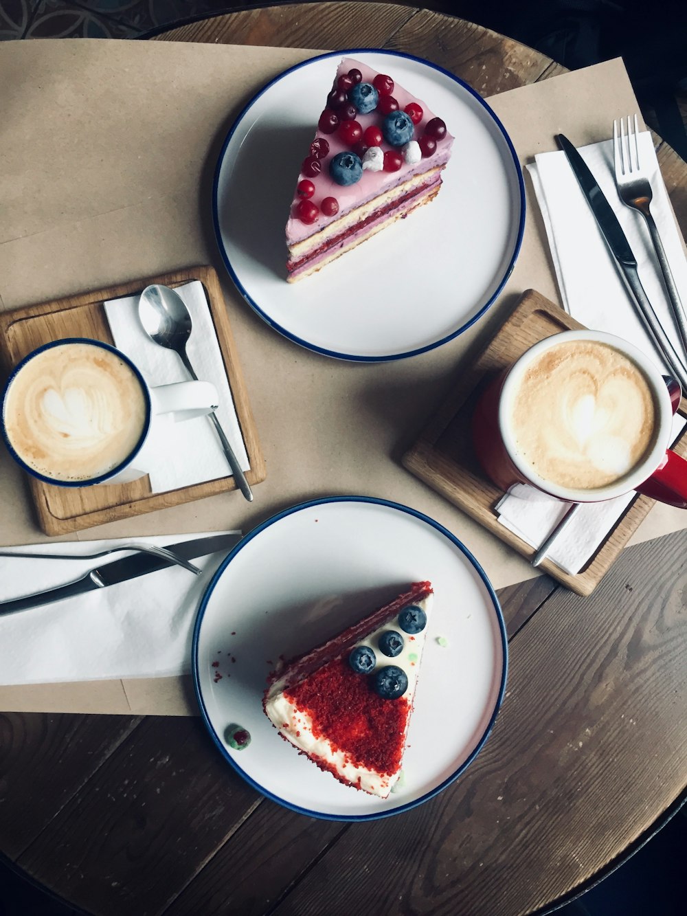 dos rebanadas de tartas de queso y arándanos y dos tazas de café con leche sobre una mesa de madera marrón