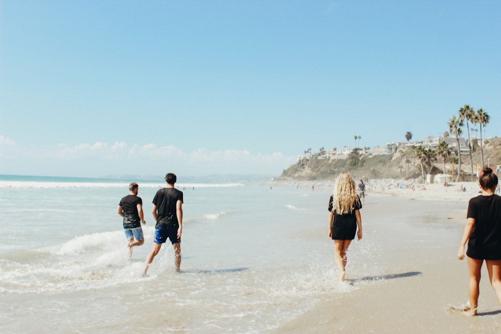 grupo de pessoas caminhando na areia ao lado do corpo d'água durante o dia