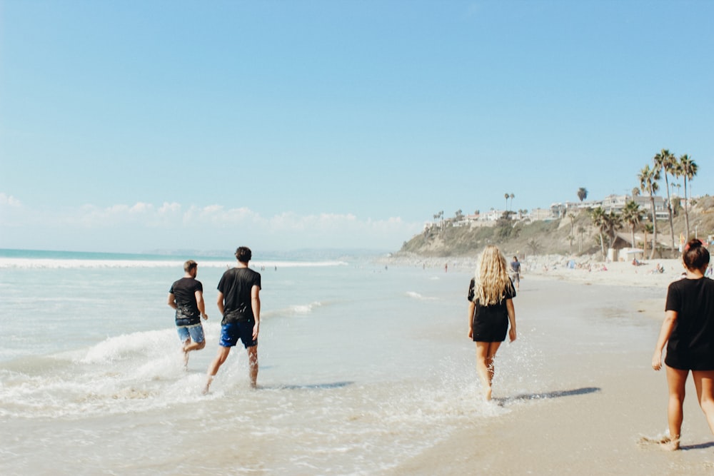 group of people walking on sand beside body of water during daytime