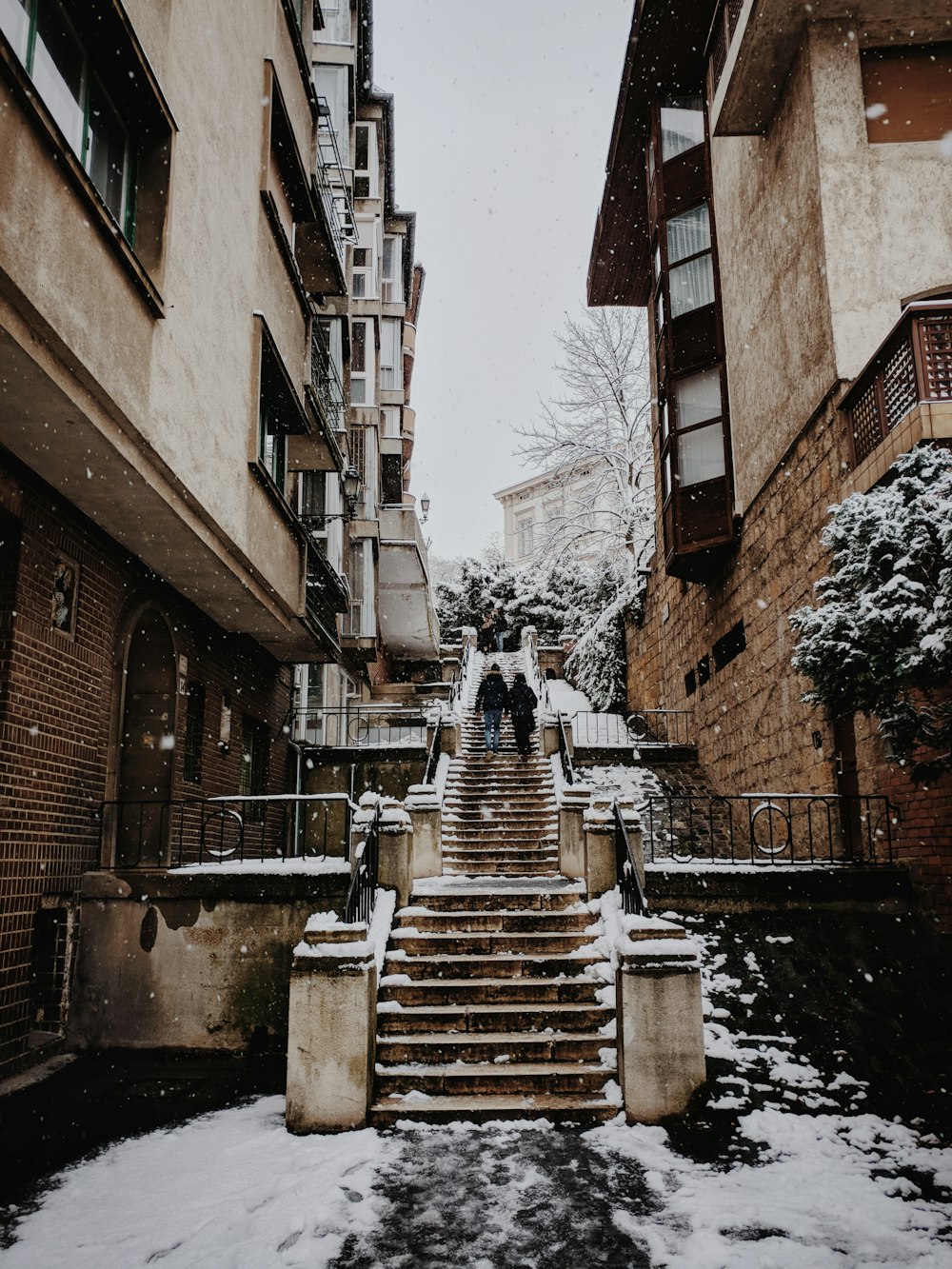 two persons walking on gray concrete stairs between buildings