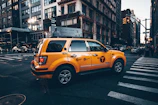 Bright yellow taxi cruising down a bustling Leeds street on a sunny day.
