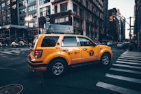 A bright yellow taxi driving through the busy streets of Kuwait City during the day.