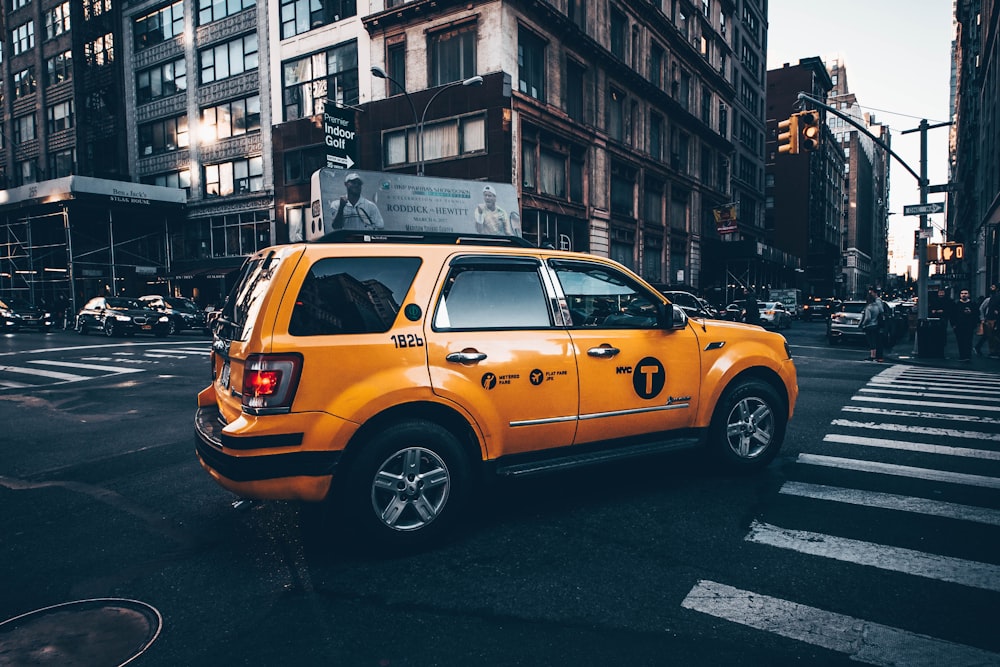 selektives Fokusfoto eines gelben Taxi-SUV, der zwischen einer von Gebäuden umgebenen Straße geparkt ist