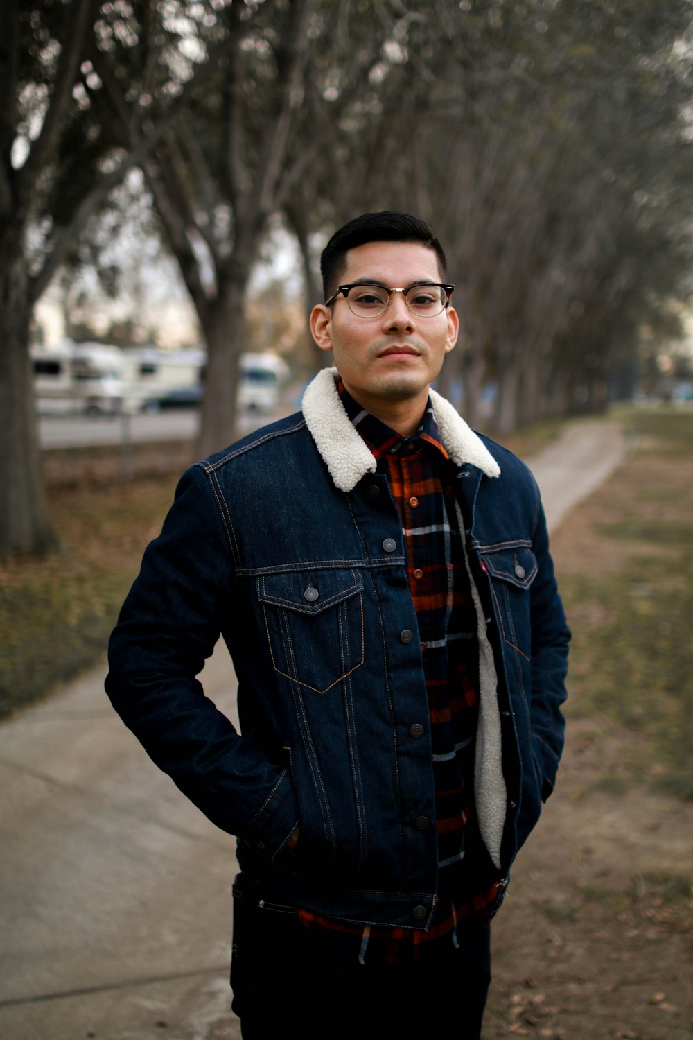 selective focus photography of man wearing blue denim jacket standing near trees