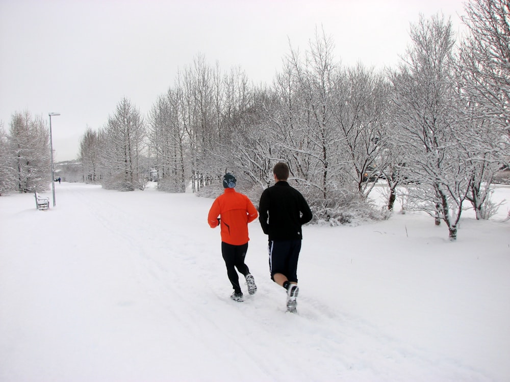 two persons running on snow field near trees