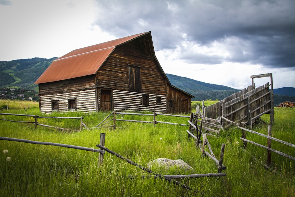 brown and white wooden barn near fence with animal during daytime