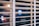 Wooden blinds partially cover a window at night, through which blurred lights from outside are visible.