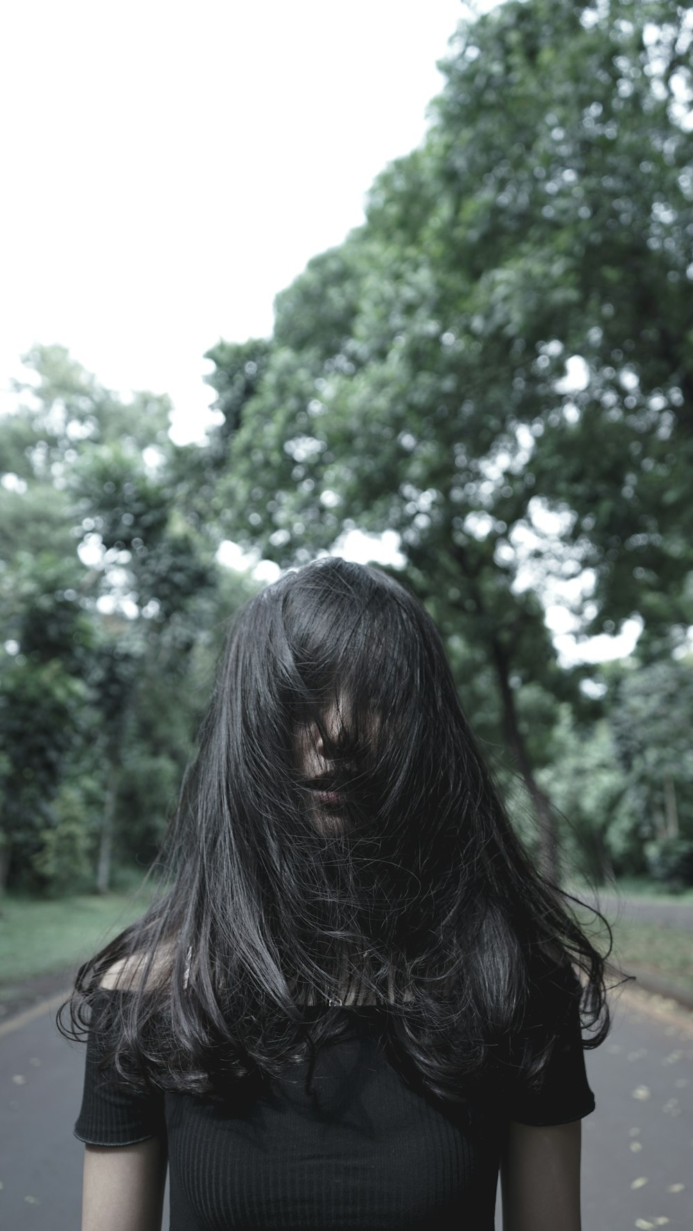 woman covering her face with her hair on road during daytime