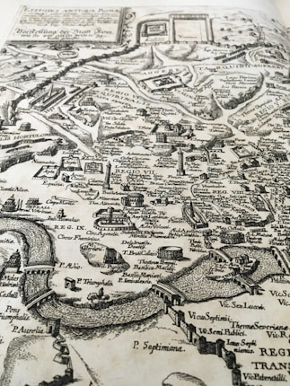 An antique map with intricate detailing, including labeled regions, landmarks, and topographical features. The map features rivers, bridges, and various structures, indicating a historical layout of a city.