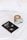 A black book titled 'Milk and Honey' by Rupi Kaur is resting on a white bedspread next to a green mug of coffee with latte art on top. The latte art features a leaf pattern, and the mug has the word 'ROAD' printed on it.