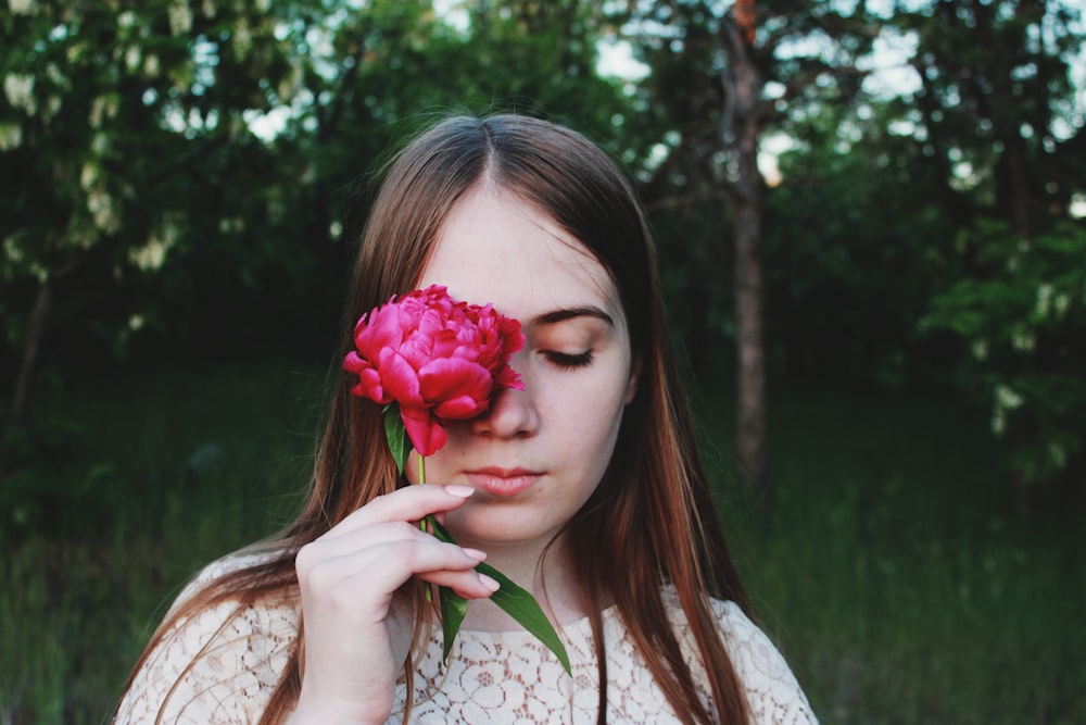 woman holding red flower over right eye